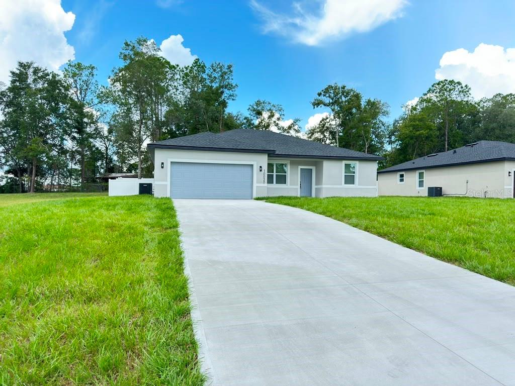 A single-story house with a gray garage, light-colored stucco exterior, and a concrete driveway — 10020 N DELTONA BOULEVARD, DUNNELLON, FL