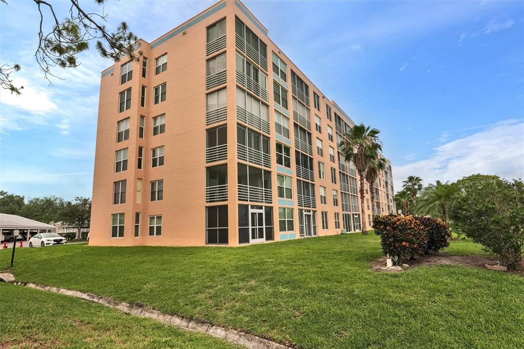A multi-story peach-colored apartment building stands on a grassy lawn with palm trees — 4570 PINEBROOK CIRCLE CIRCLE UNIT 404, BRADENTON, FL