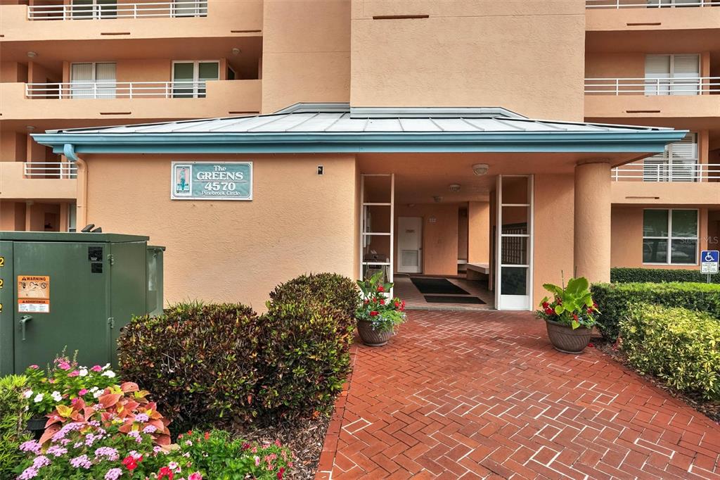 The exterior of a multi-story apartment building features a brick walkway leading to the entrance — 4570 PINEBROOK CIRCLE CIRCLE UNIT 404, BRADENTON, FL