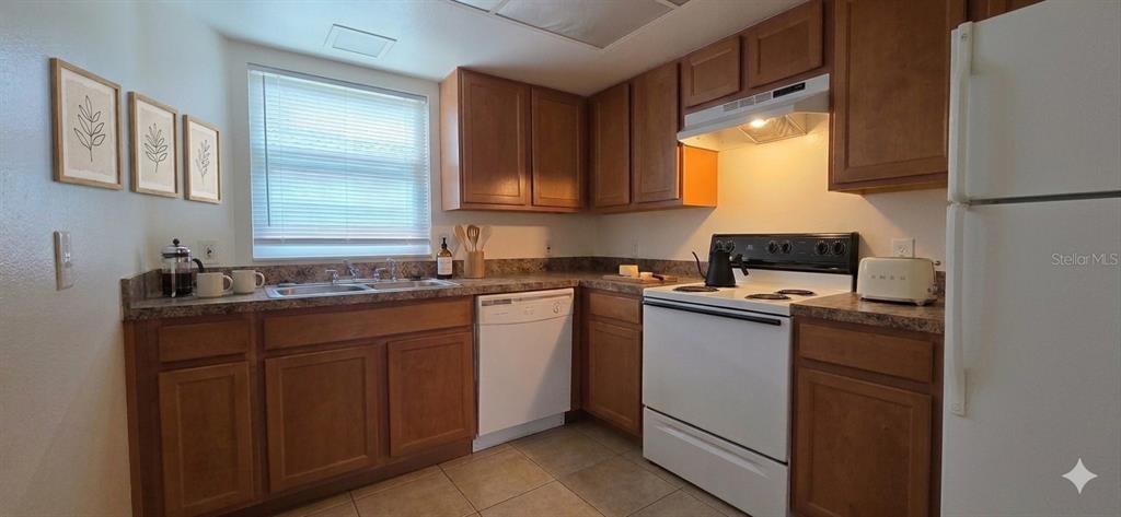 A kitchen features wood cabinets, white appliances, tiled countertops, and a window with blinds — 2820 DUPONT STREET S UNIT 201, GULFPORT, FL