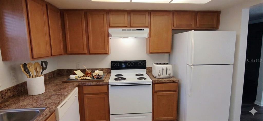 A kitchen features wood cabinets, laminate countertops, a white stove, and a white refrigerator — 2820 DUPONT STREET S UNIT 201, GULFPORT, FL