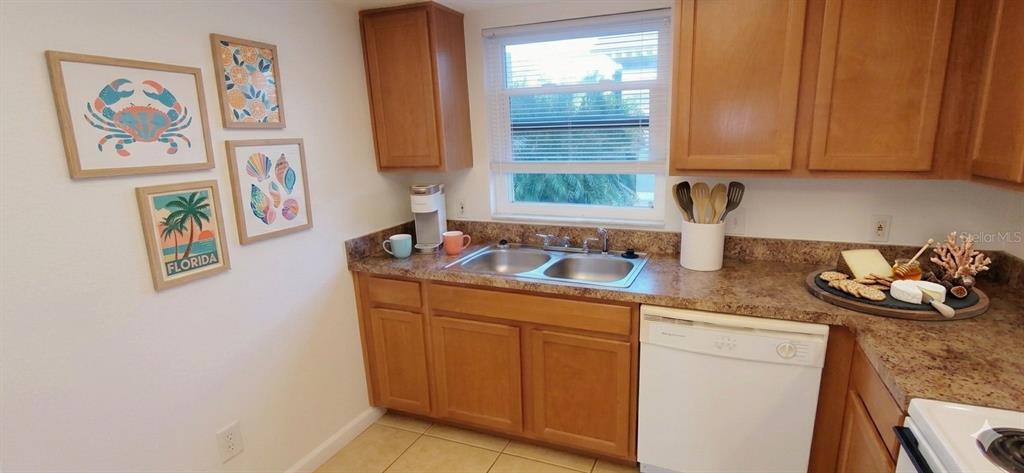 A kitchen features wooden cabinets, a double sink, a dishwasher, and framed coastal wall art — 2820 DUPONT STREET S UNIT 201, GULFPORT, FL