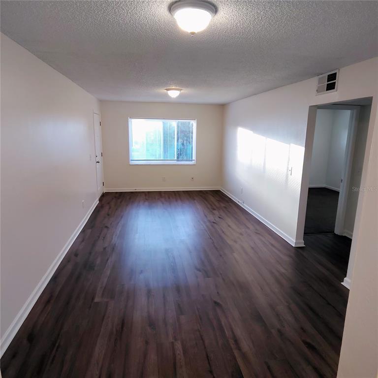 An empty room features dark wood-look flooring, light-colored walls, two ceiling lights, and a window — 2820 DUPONT STREET S UNIT 201, GULFPORT, FL