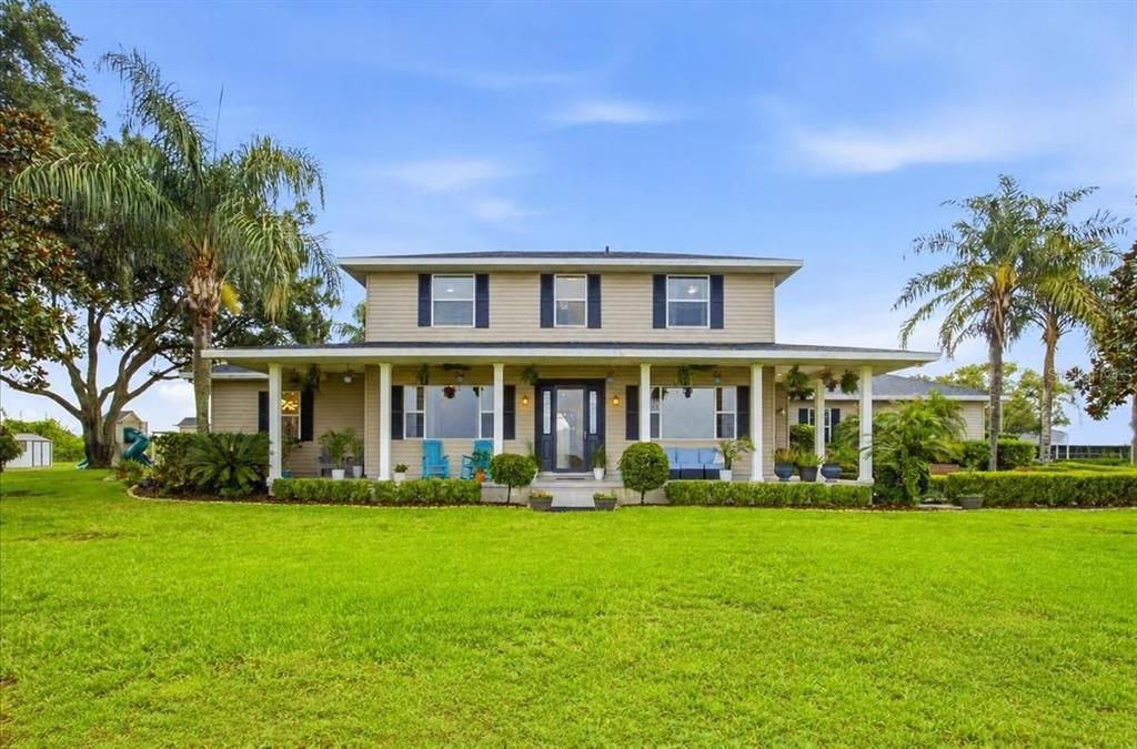 A beige two-story house features a covered porch, a concrete patio, and wooden outdoor furniture — 915 N CROOKED LAKE DRIVE, BABSON PARK, FL