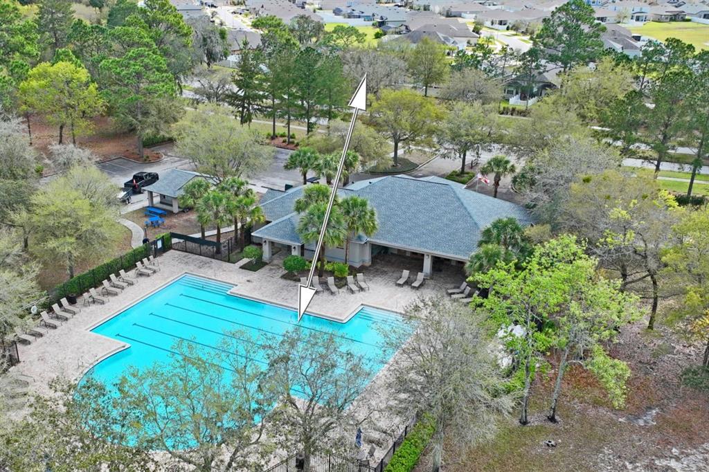 An aerial view shows a community swimming pool and clubhouse surrounded by trees and landscaping — 571 OLD WINDSOR WAY, SPRING HILL, FL
