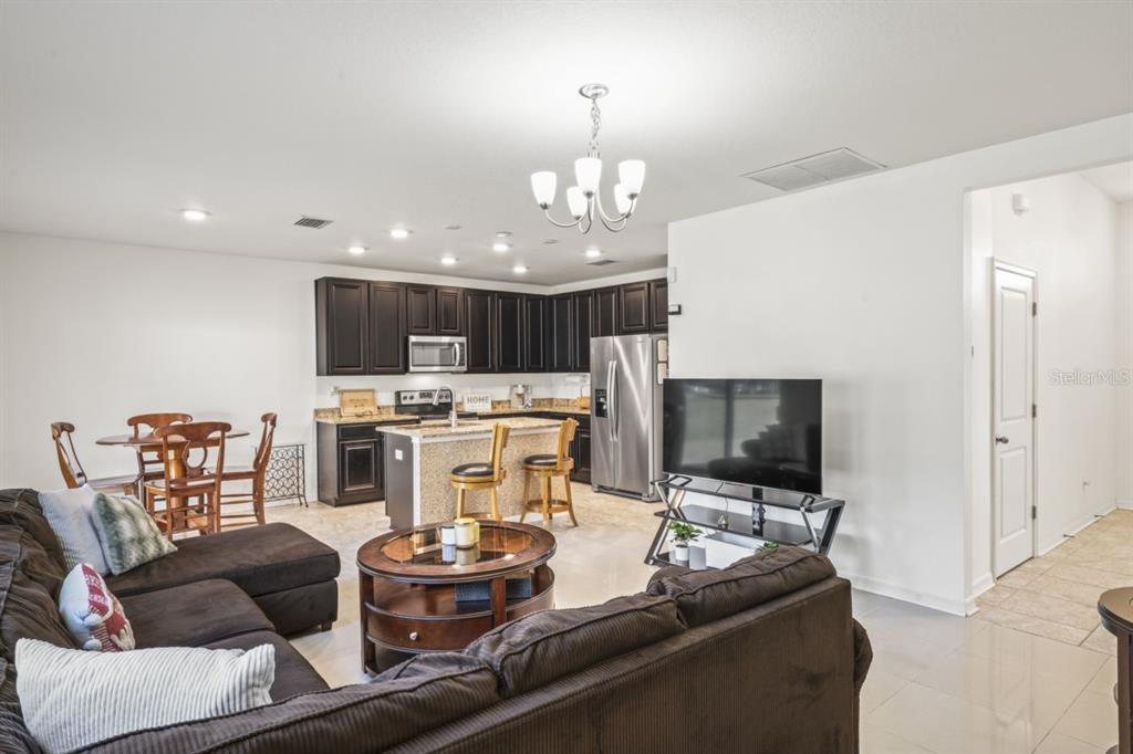 An open-concept living room and kitchen featuring dark cabinetry, granite countertops, and tile flooring — 571 OLD WINDSOR WAY, SPRING HILL, FL