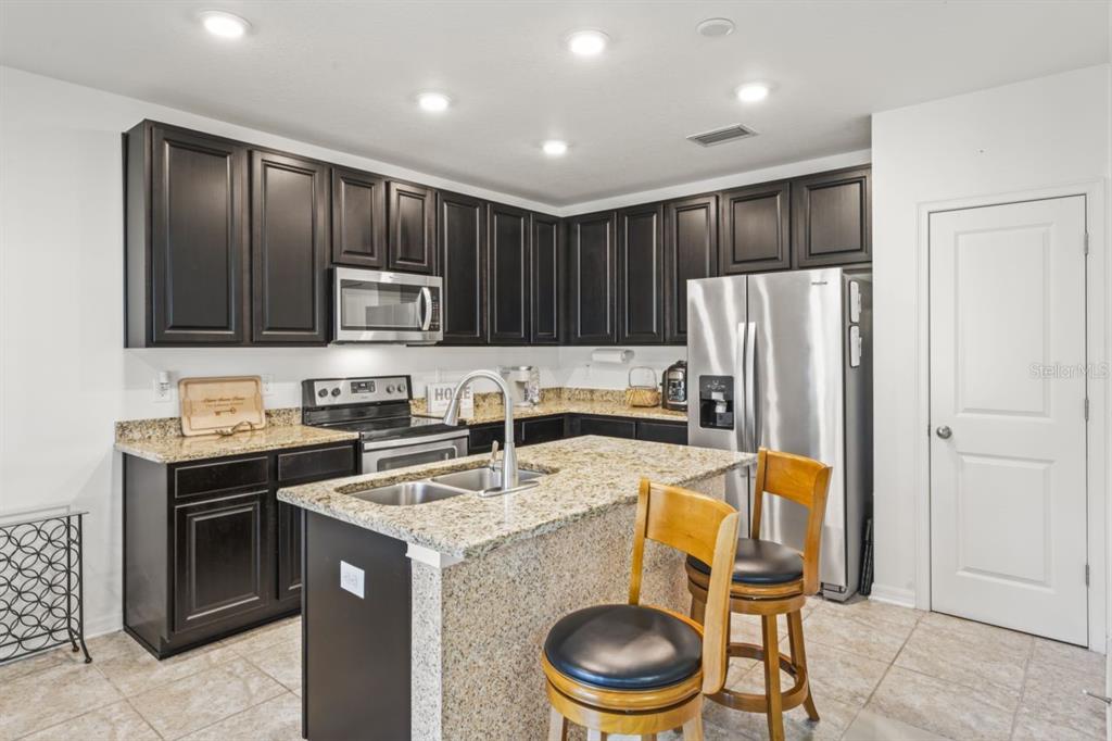 A kitchen features dark wood cabinets, granite countertops, stainless steel appliances, and a center island — 571 OLD WINDSOR WAY, SPRING HILL, FL