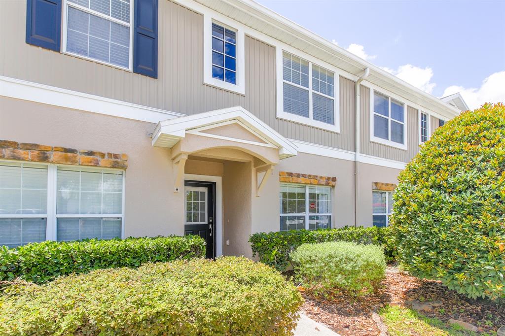 A two-story townhouse exterior features beige siding, a covered entryway, and manicured landscaping — 16342 ROLLINGBROOK DRIVE, ODESSA, FL