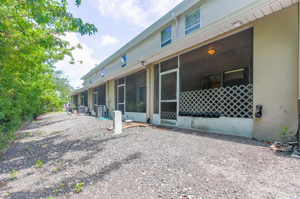 The rear exterior of a multi-unit townhouse features screened-in patios and a gravel yard — 16342 ROLLINGBROOK DRIVE, ODESSA, FL