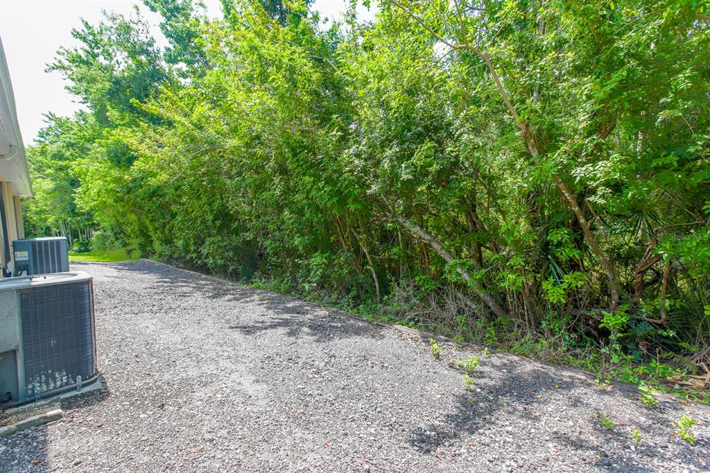 A gravel side yard runs alongside a house with an air conditioning unit — 16342 ROLLINGBROOK DRIVE, ODESSA, FL