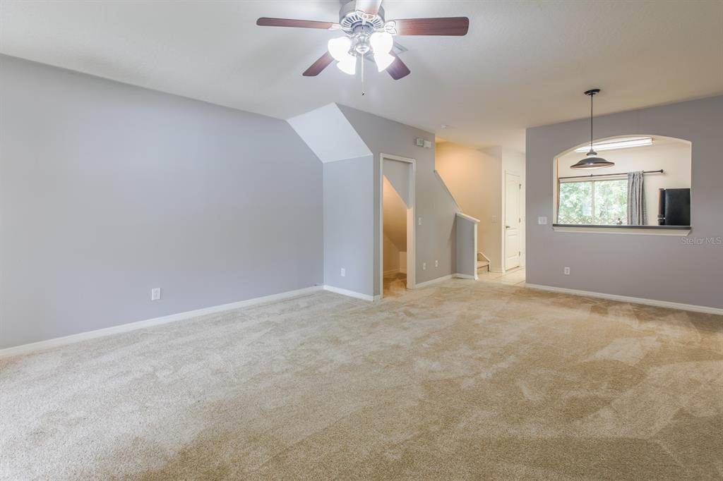 A carpeted living room features a ceiling fan, a staircase, and a kitchen pass-through window — 16342 ROLLINGBROOK DRIVE, ODESSA, FL