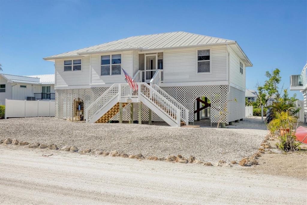 A white elevated house with a metal roof and lattice skirting stands on a gravel lot — 271 BOCILLA DRIVE, PLACIDA, FL