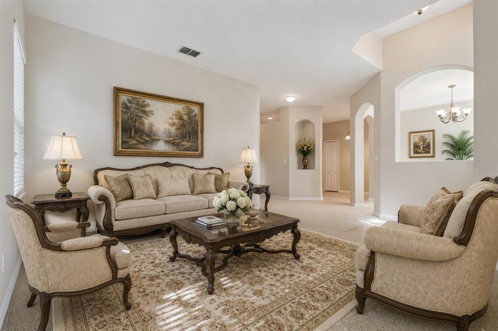 A formal living room features beige furniture, a patterned area rug, and arched wall niches — 2925 DAYTON DRIVE, WINTER HAVEN, FL