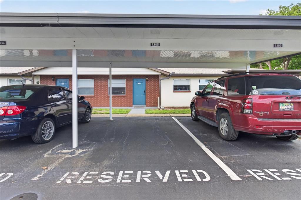 A covered parking area with two reserved spaces sits in front of a brick apartment building — 24862 US HIGHWAY 19 N UNIT 3305, CLEARWATER, FL