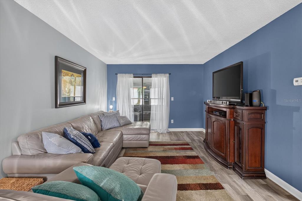 A living room features a grey sectional sofa, a wooden media console, and blue walls — 24862 US HIGHWAY 19 N UNIT 3305, CLEARWATER, FL
