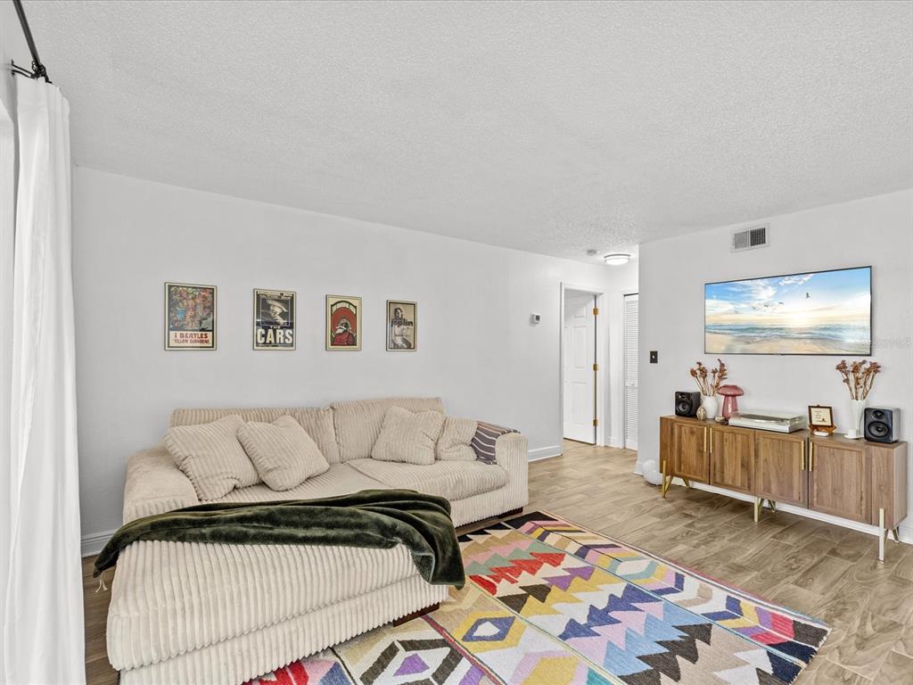 A living room features a beige sectional sofa, a colorful rug, and wall-mounted music posters — 8653 MALLARD RESERVE DRIVE UNIT 103, TAMPA, FL