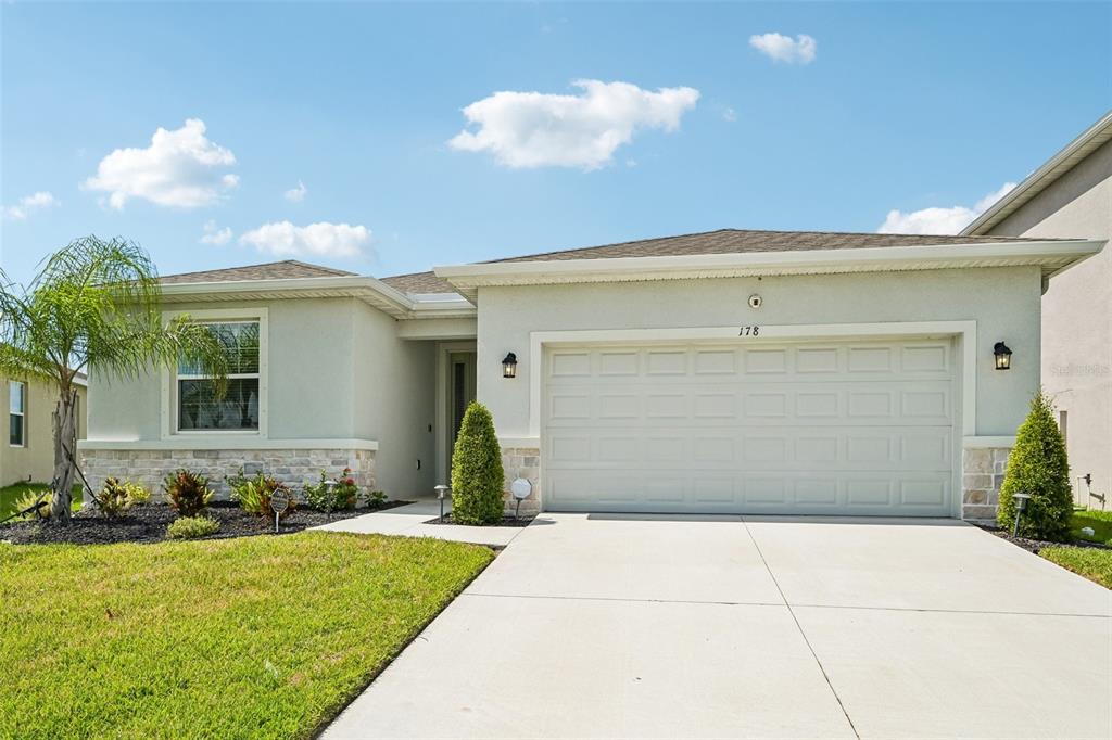 A single-story house with a light-colored stucco exterior, stone accents, and a two-car garage — 178 MANGROVE MANOR DRIVE, APOLLO BEACH, FL