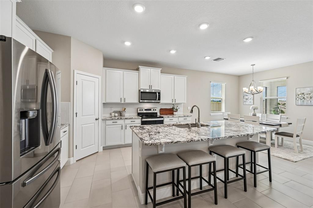 A kitchen features white cabinets, granite countertops, a center island with stools, and tile flooring — 178 MANGROVE MANOR DRIVE, APOLLO BEACH, FL