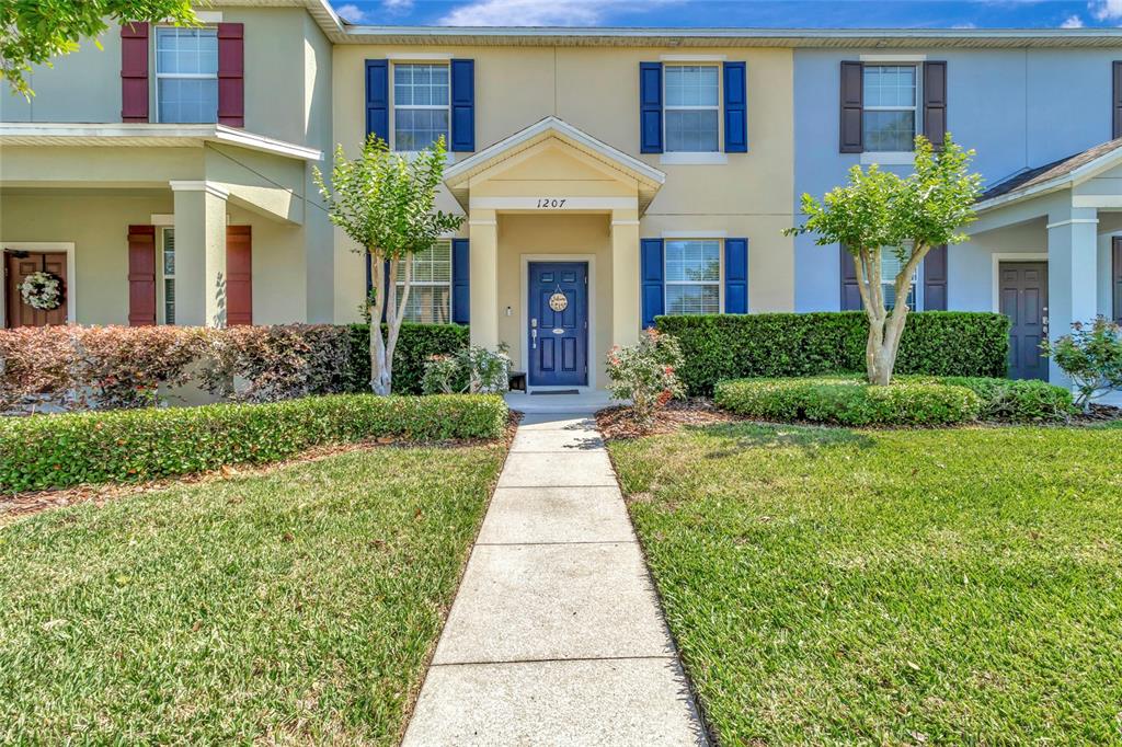 A two-story townhouse exterior with a blue front door, shutters, and a concrete walkway — 1207 ALSTON BAY BOULEVARD, APOPKA, FL