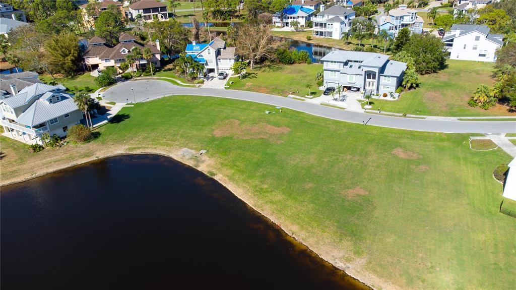 An aerial view shows a large grassy lot situated between a curved road and water — 85 SANDPIPER POINTE, TARPON SPRINGS, FL