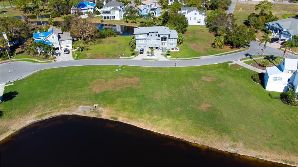 An aerial view shows a large, vacant grassy lot situated between a lake and road — 85 SANDPIPER POINTE, TARPON SPRINGS, FL