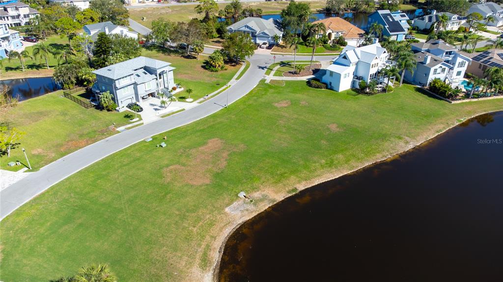 An aerial view shows a vacant grassy lot situated between a road and a lake — 85 SANDPIPER POINTE, TARPON SPRINGS, FL