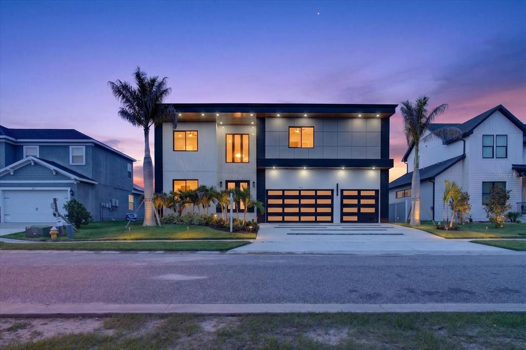 A modern two-story house with a flat roof, dark trim, and a three-car garage at dusk — 3420 CHANNELSIDE COURT, SAFETY HARBOR, FL