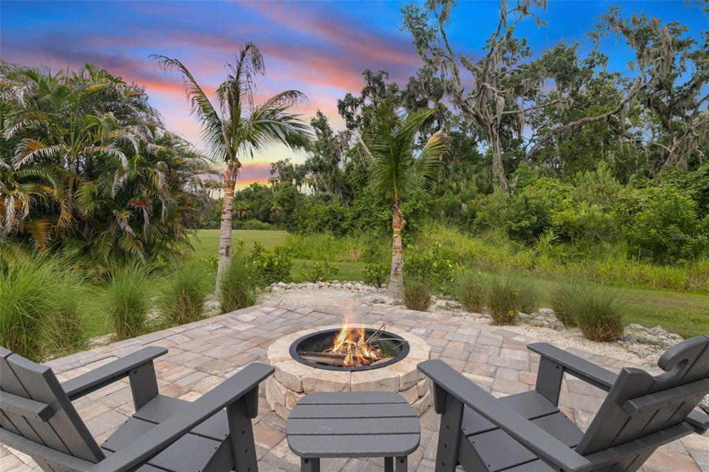A stone fire pit sits on a paved patio with two chairs overlooking a grassy yard — 5512 74TH PLACE E, ELLENTON, FL