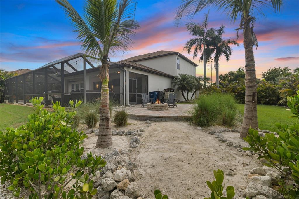 A backyard features a stone fire pit, a screened-in patio, and palm trees at sunset — 5512 74TH PLACE E, ELLENTON, FL