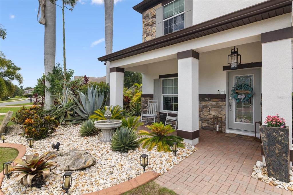 A stone-accented house exterior features a covered porch, a stone fountain, and desert-style landscaping — 5512 74TH PLACE E, ELLENTON, FL