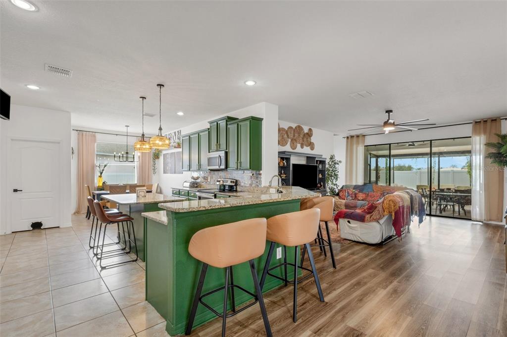 An open-concept kitchen with green cabinets and a breakfast bar overlooks a living area — 611 WABASH BREEZE CIRCLE, RUSKIN, FL