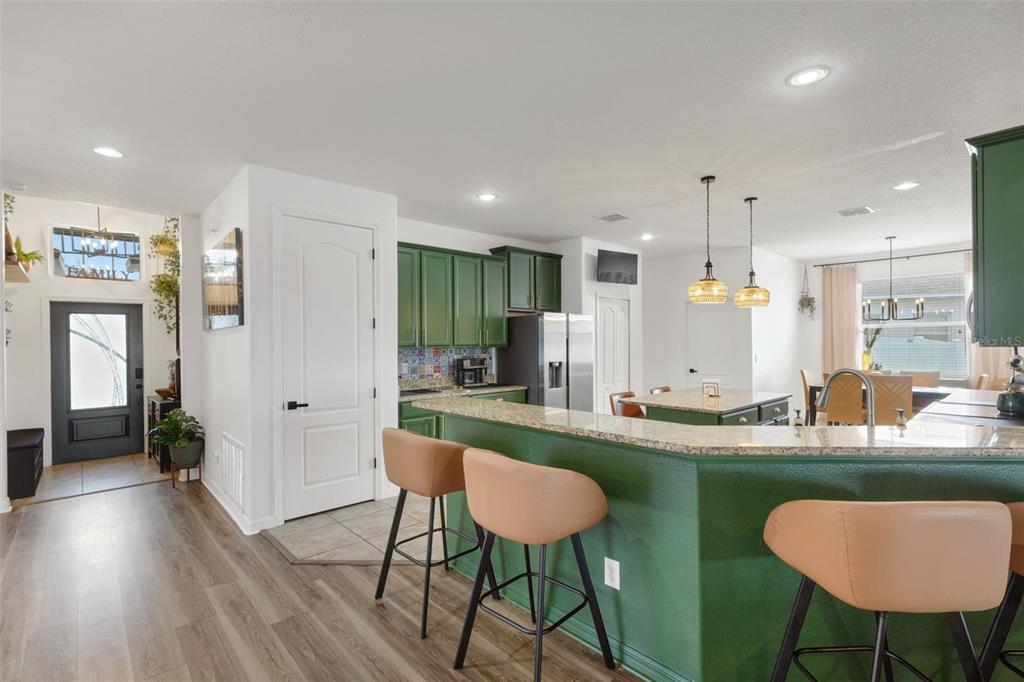 A kitchen with green cabinets, a granite-topped island, and bar stools on wood flooring — 611 WABASH BREEZE CIRCLE, RUSKIN, FL