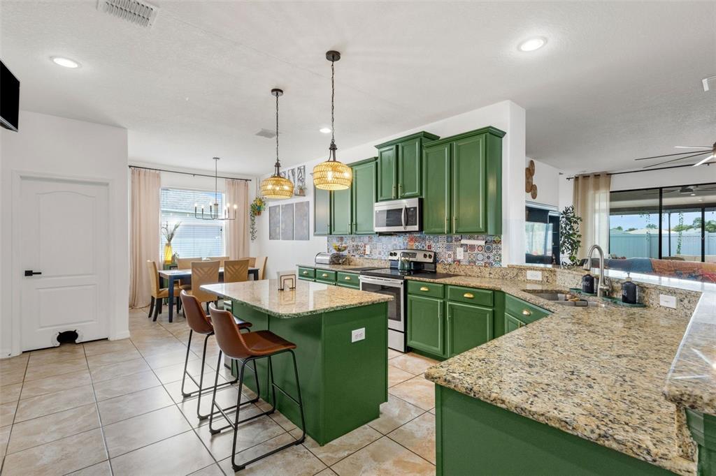 A kitchen features green cabinets, granite countertops, a central island, and a patterned tile backsplash — 611 WABASH BREEZE CIRCLE, RUSKIN, FL