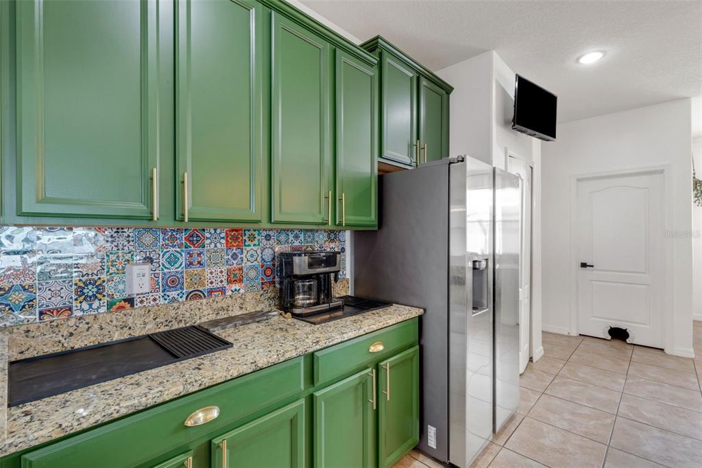 A kitchen features green cabinets, a colorful patterned backsplash, granite countertops, and stainless steel appliances — 611 WABASH BREEZE CIRCLE, RUSKIN, FL