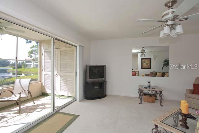 A living room features a ceiling fan, a television on a stand, and a sliding glass door — 7153 W COUNTRY CLUB DRIVE N UNIT 146, SARASOTA, FL
