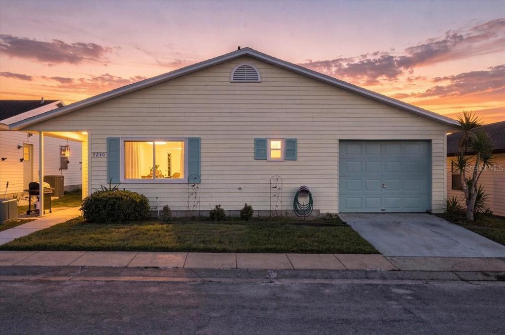 A single-story house with light yellow siding, blue shutters, and an attached garage at sunset — 2240 SEA ISLAND CIRCLE N, LAKELAND, FL