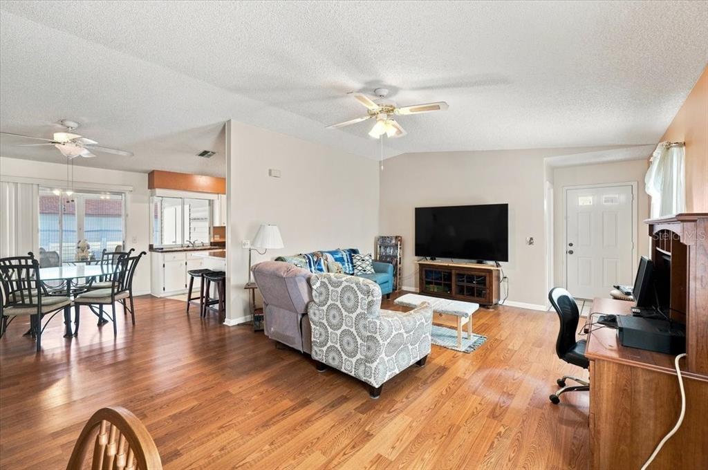 A living room with hardwood floors, a ceiling fan, a television, and an adjacent kitchen — 2240 SEA ISLAND CIRCLE N, LAKELAND, FL