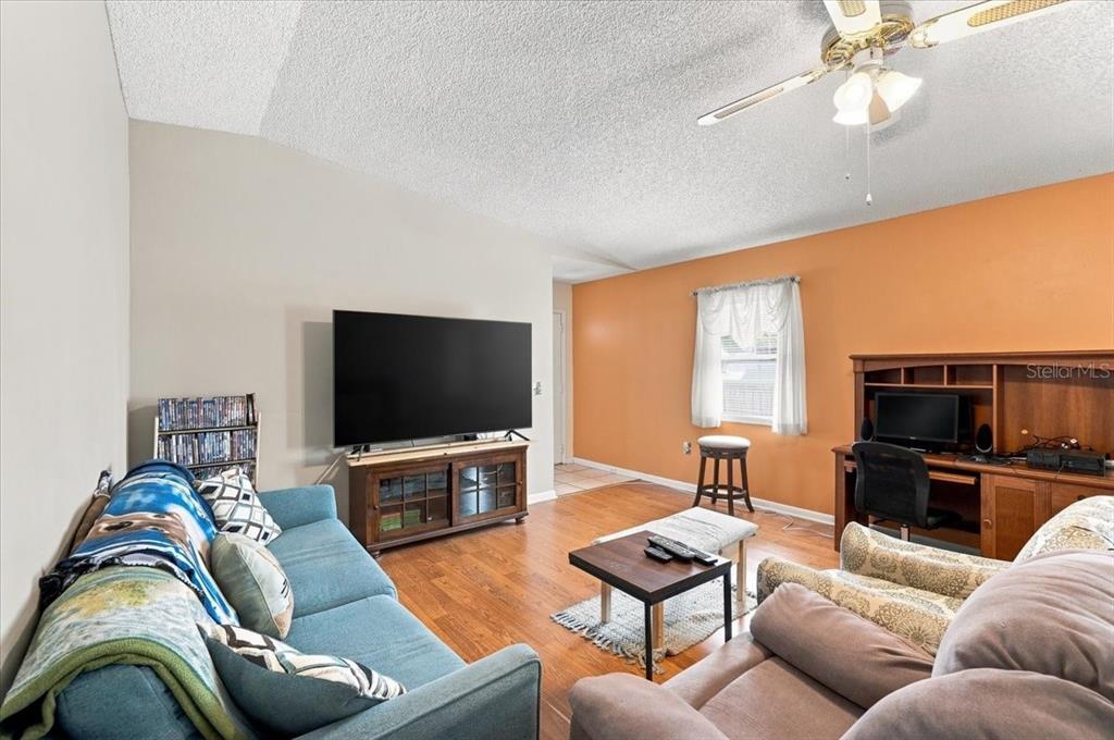 A living room features a blue sofa, a television on a wooden stand, and orange walls — 2240 SEA ISLAND CIRCLE N, LAKELAND, FL