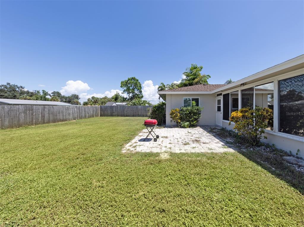 A backyard features a paved patio, a red grill, and a wooden fence under blue skies — 2161 INNER CASS CIRCLE, SARASOTA, FL