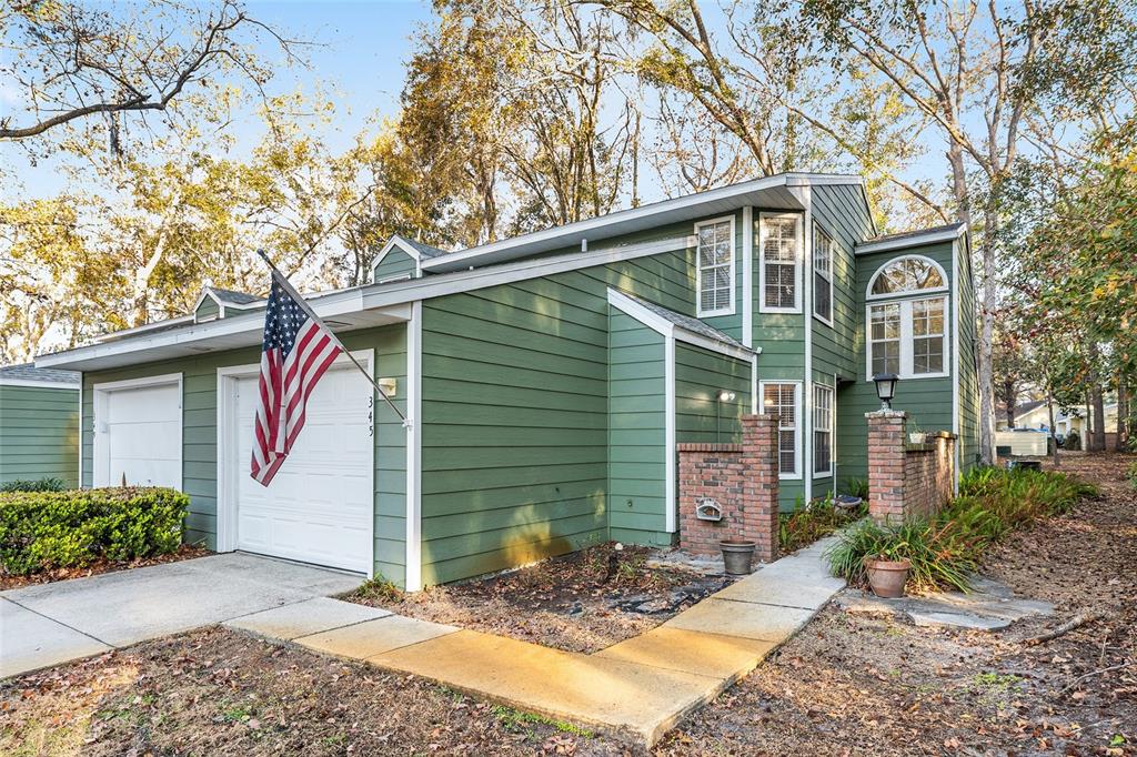 A two-story green house with a garage, an American flag, and a brick entryway — 345 NW 48TH BOULEVARD UNIT K, GAINESVILLE, FL
