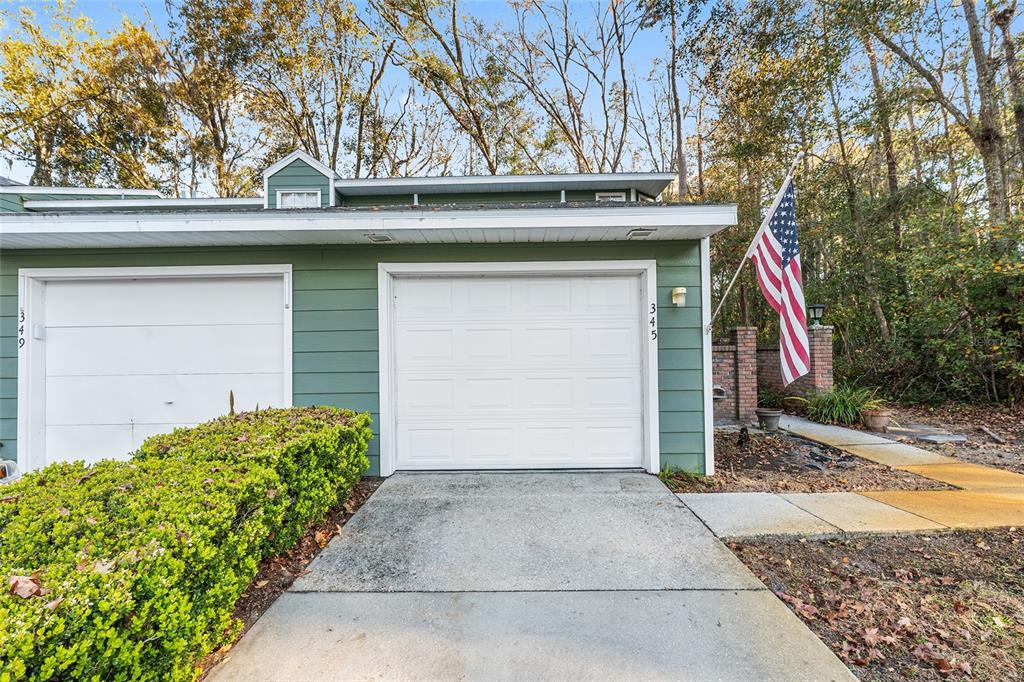A green house exterior features two garage doors, a concrete driveway, and an American flag — 345 NW 48TH BOULEVARD UNIT K, GAINESVILLE, FL