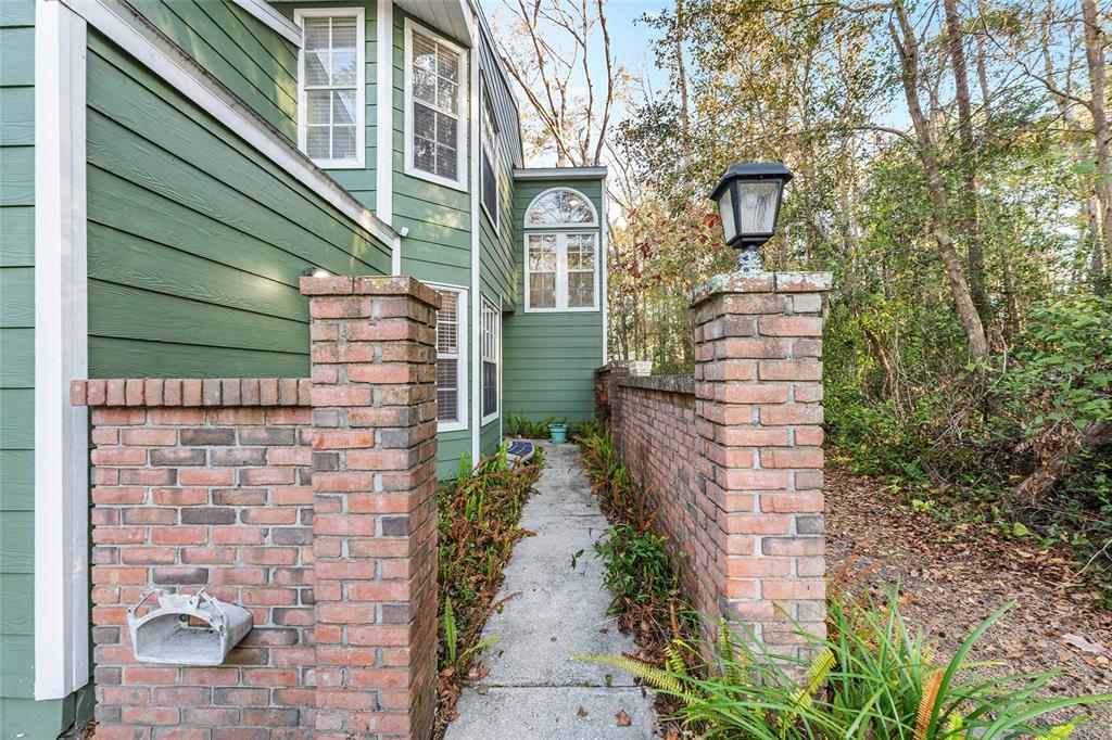 A concrete walkway leads between two brick pillars toward the side of a green house — 345 NW 48TH BOULEVARD UNIT K, GAINESVILLE, FL
