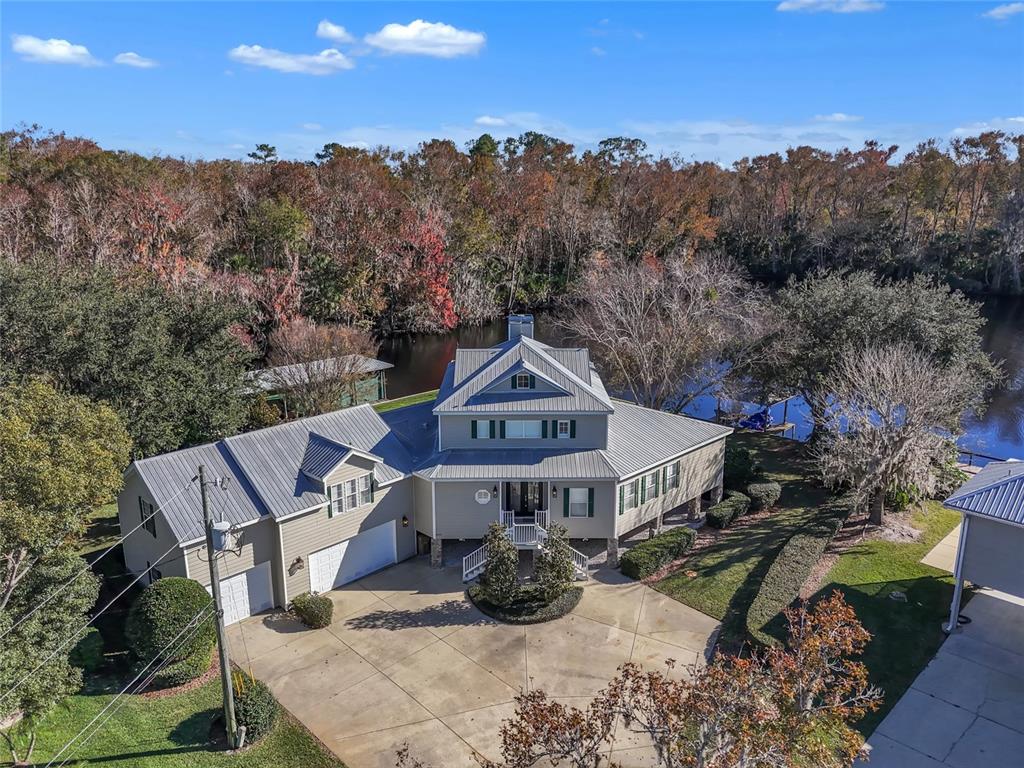 An aerial view shows a multi-story house with a metal roof, garage, and waterfront backyard — 56633 OTTER ROAD, ASTOR, FL