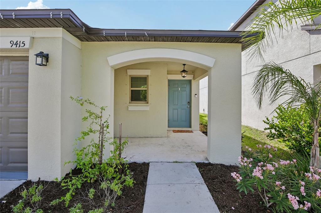 A beige house exterior features a covered entryway, a blue front door, and a walkway — 9415 LEMON DROP LOOP, SUN CITY CENTER, FL