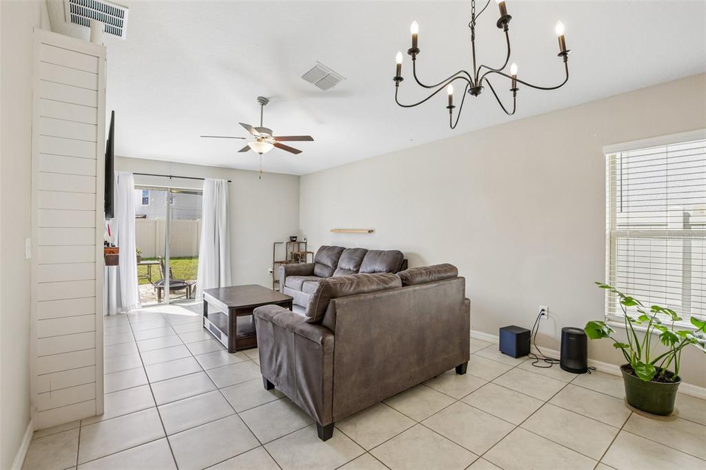 A living room features tile flooring, a brown sofa, a chandelier, and a sliding glass door — 9415 LEMON DROP LOOP, SUN CITY CENTER, FL