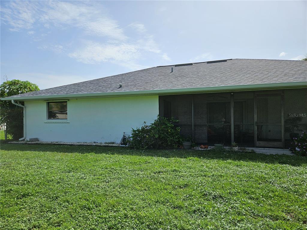 The exterior of a house features a white wall, a screened-in porch, and a shingled roof — 25358 AYSEN DRIVE, PUNTA GORDA, FL