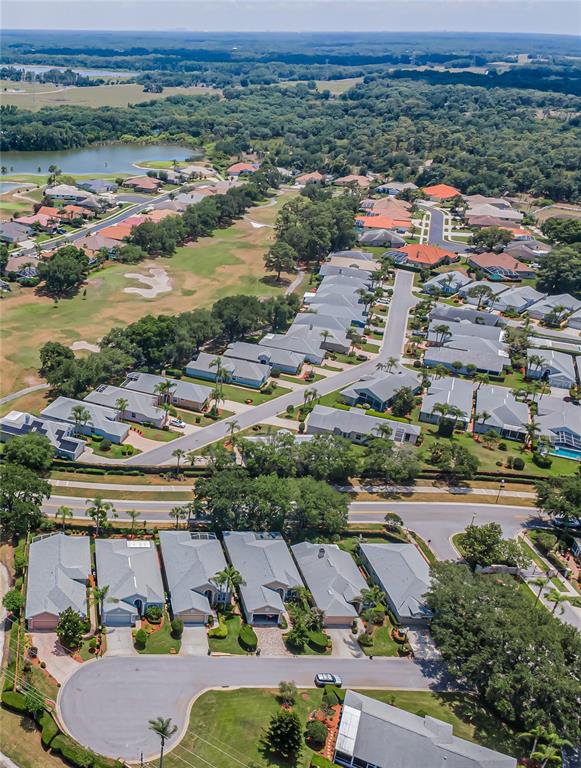 An aerial view shows a suburban neighborhood with houses, a golf course, and a lake — 9310 SOUCHAK DRIVE, TRINITY, FL