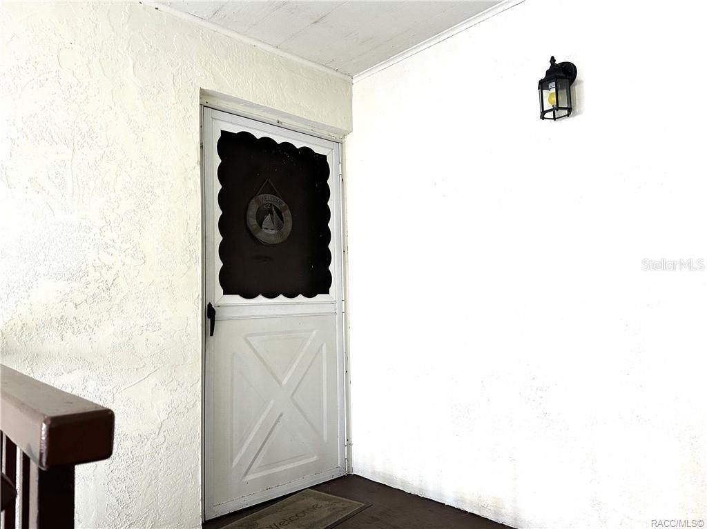 A white exterior door with a screen and a wall-mounted light fixture on a porch — 2400 FOREST DRIVE UNIT 227, INVERNESS, FL