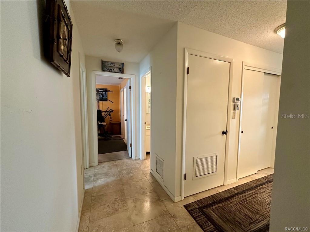 A hallway with tile flooring leads to a room containing exercise equipment and a bathroom — 2400 FOREST DRIVE UNIT 227, INVERNESS, FL