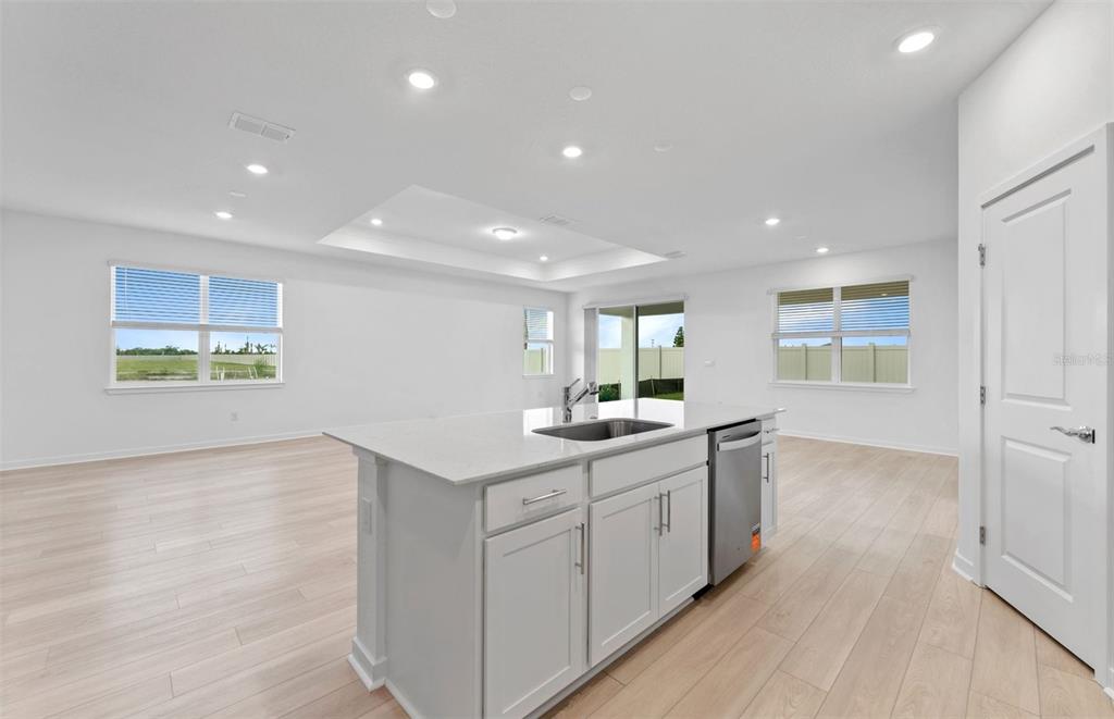 A bright open-concept living room and kitchen featuring white cabinetry, wood-look flooring, and sliding doors — 16816 HARMONY RIVER LANE, PARRISH, FL